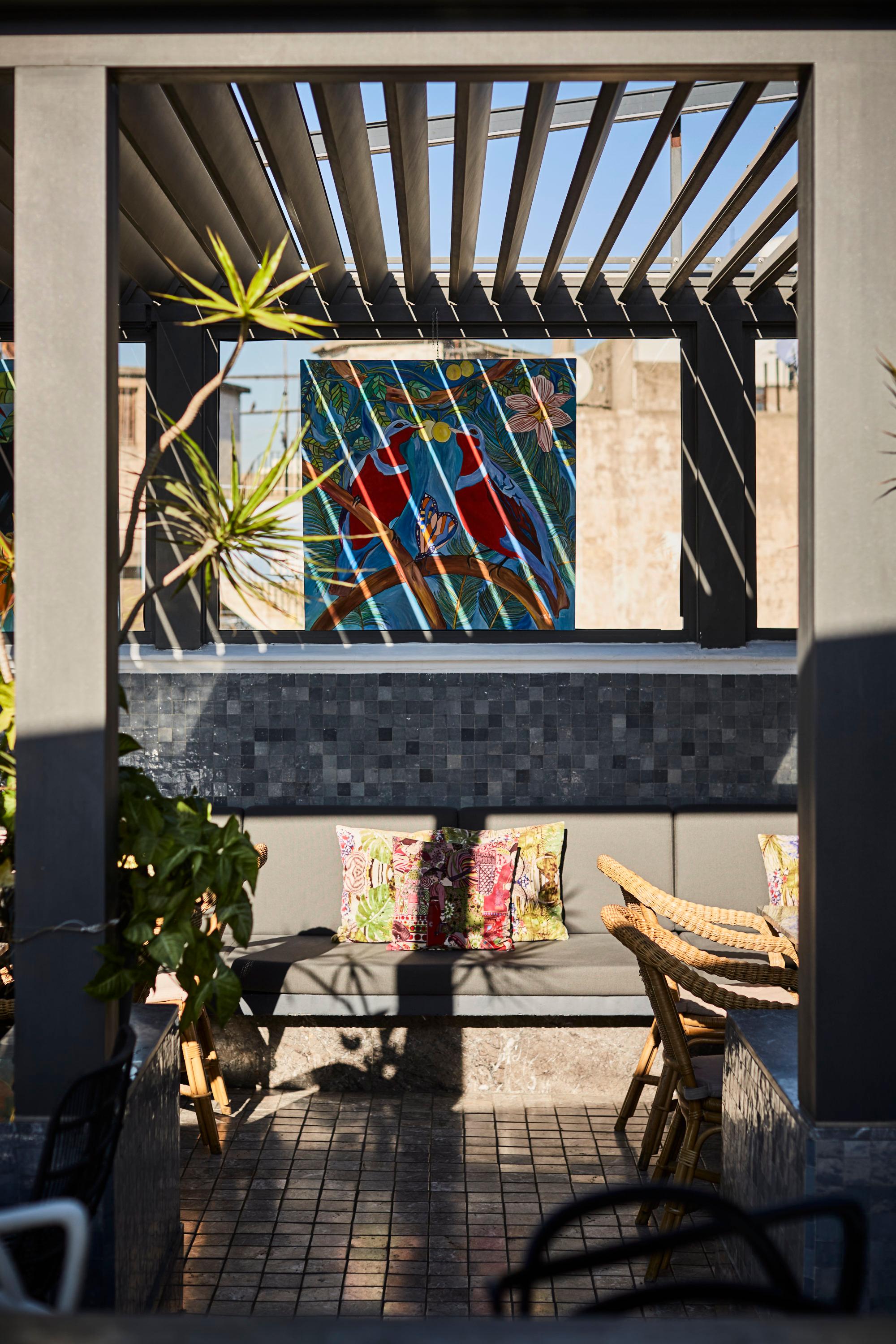 Rooftop terrace at Le Doge Hotel with a heart mural, patterned cushions, and bamboo chair under a metal pergola