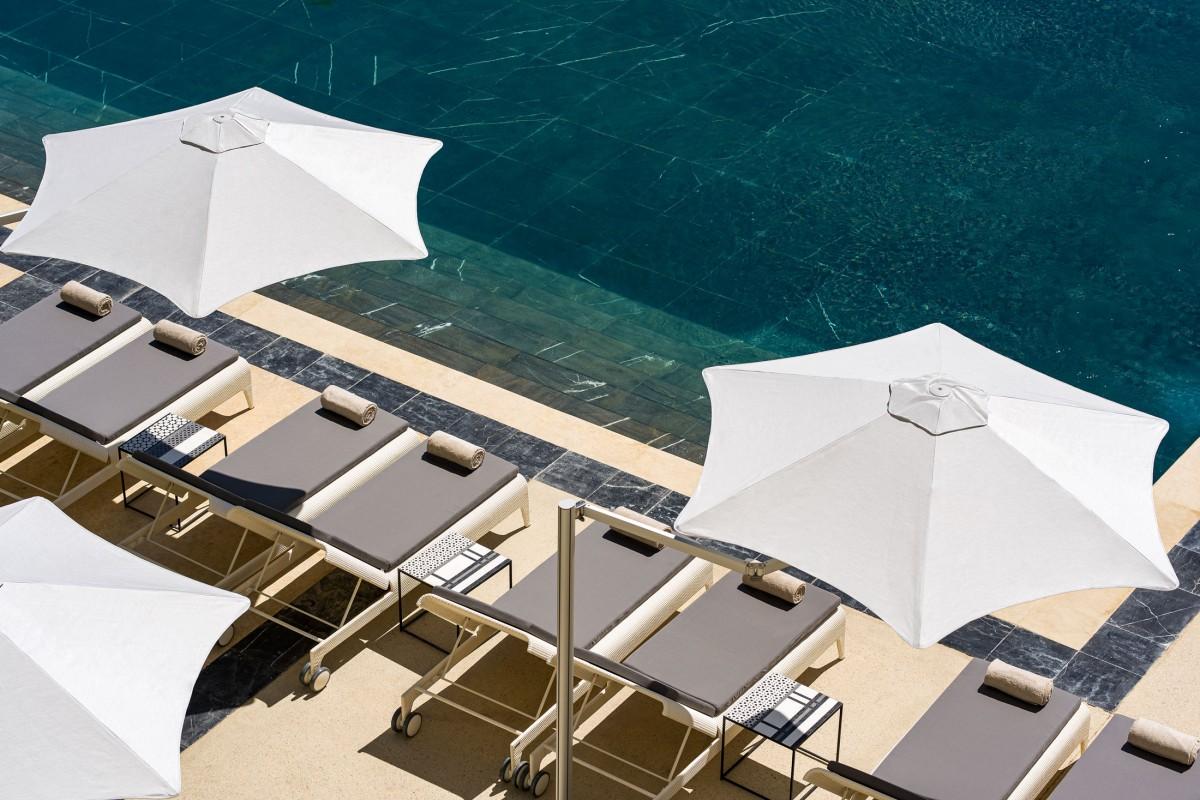 Poolside loungers under white umbrellas await guests at the Fairmont Tazi Palace, offering a view of clear turquoise waters.