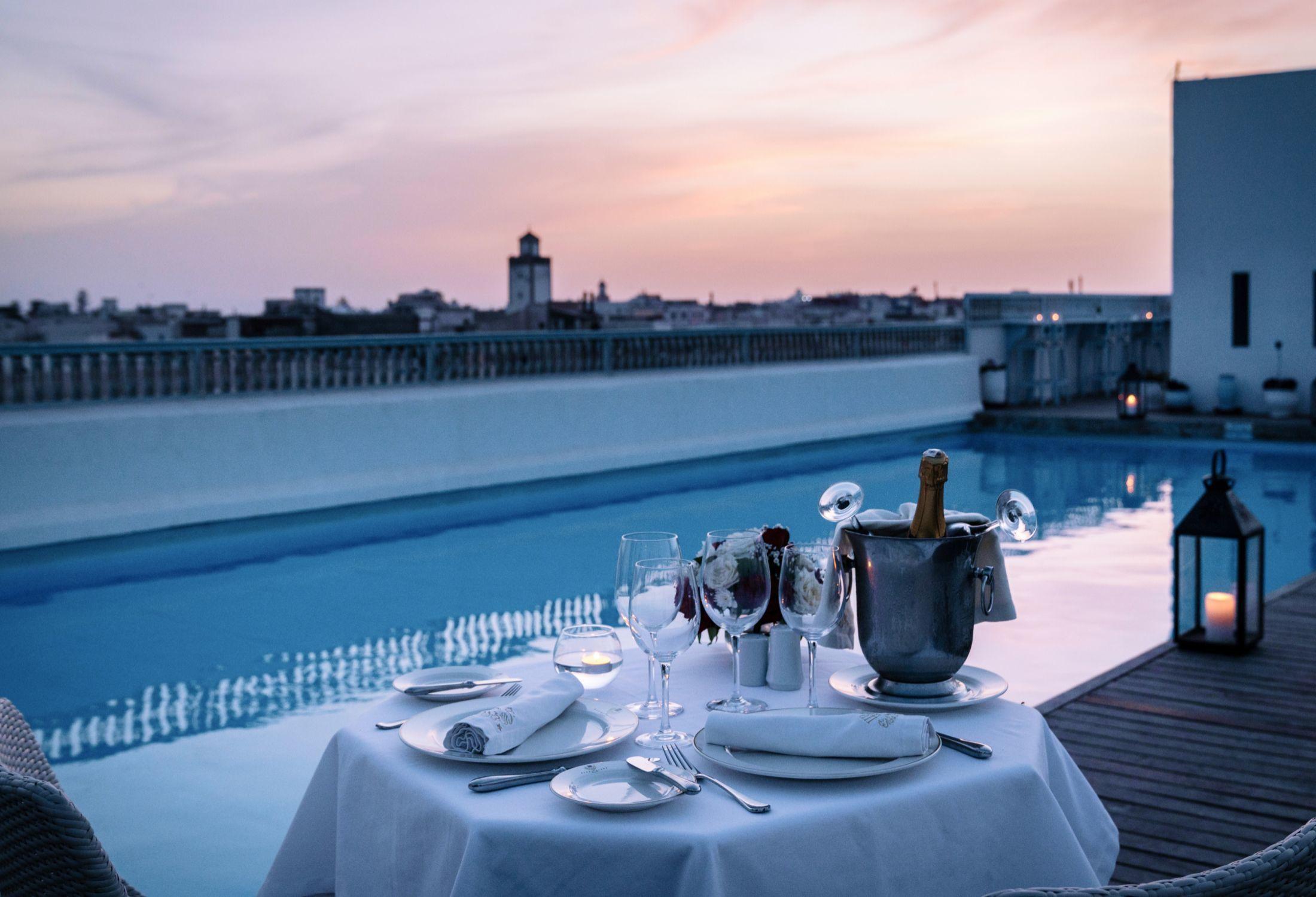 Rooftop poolside dining at dusk with a set table and skyline view at L\'Heure Bleue Palais