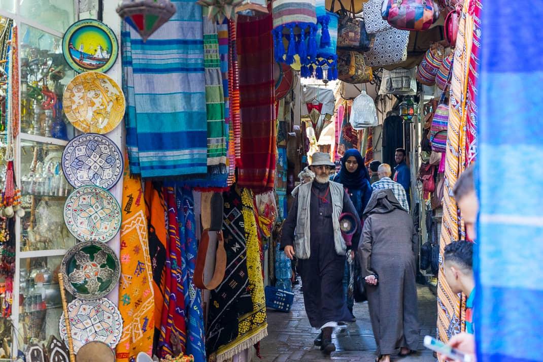 A vibrant scene in the old Medina of Tangier  where locals and visitors browse stalls brimming with colorful textiles, handcrafted pottery, and other unique goods.