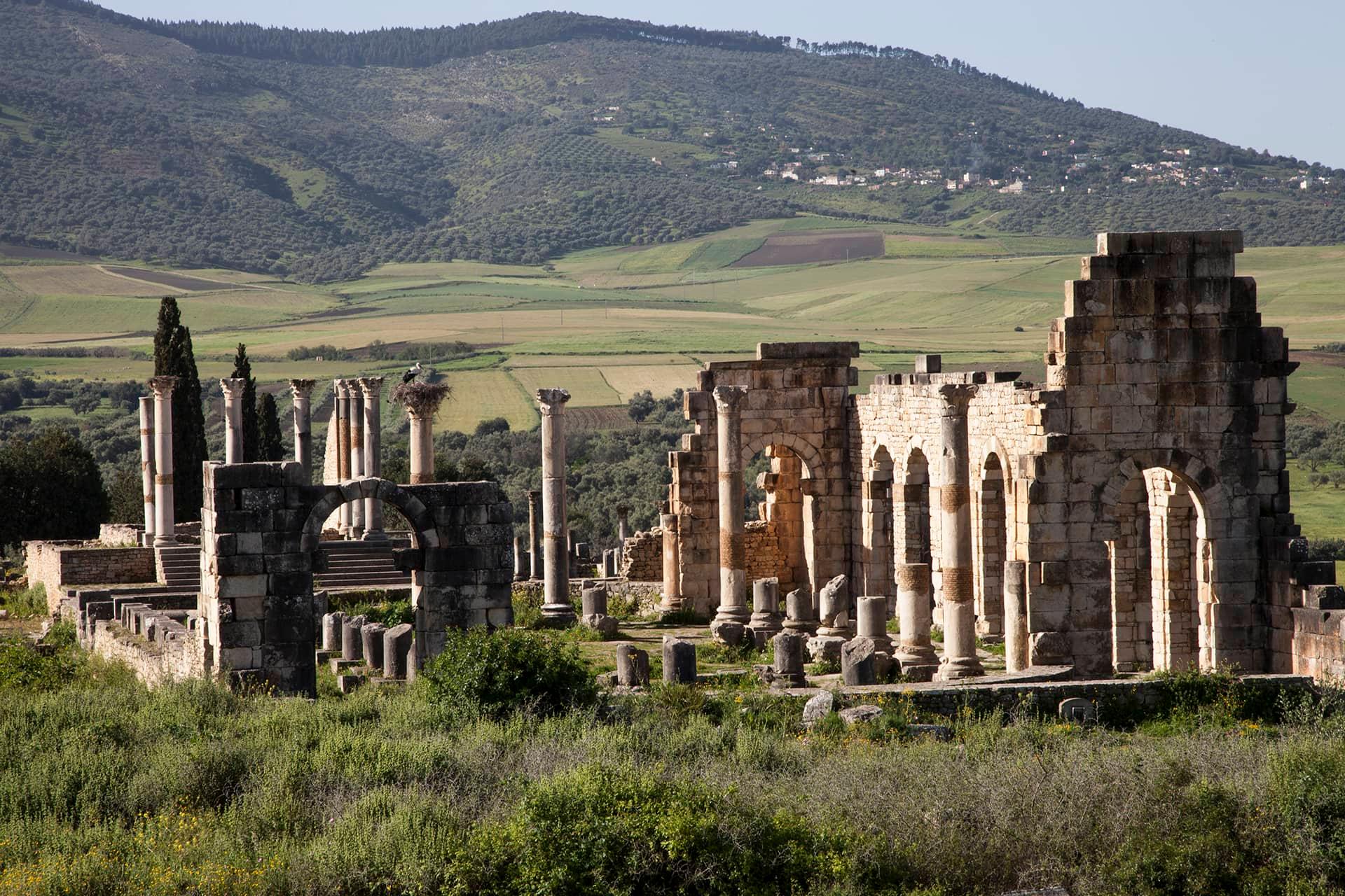 The ancient Roman ruins of Volubilis, Morocco, stand in majestic solitude against a backdrop of rolling green hills.