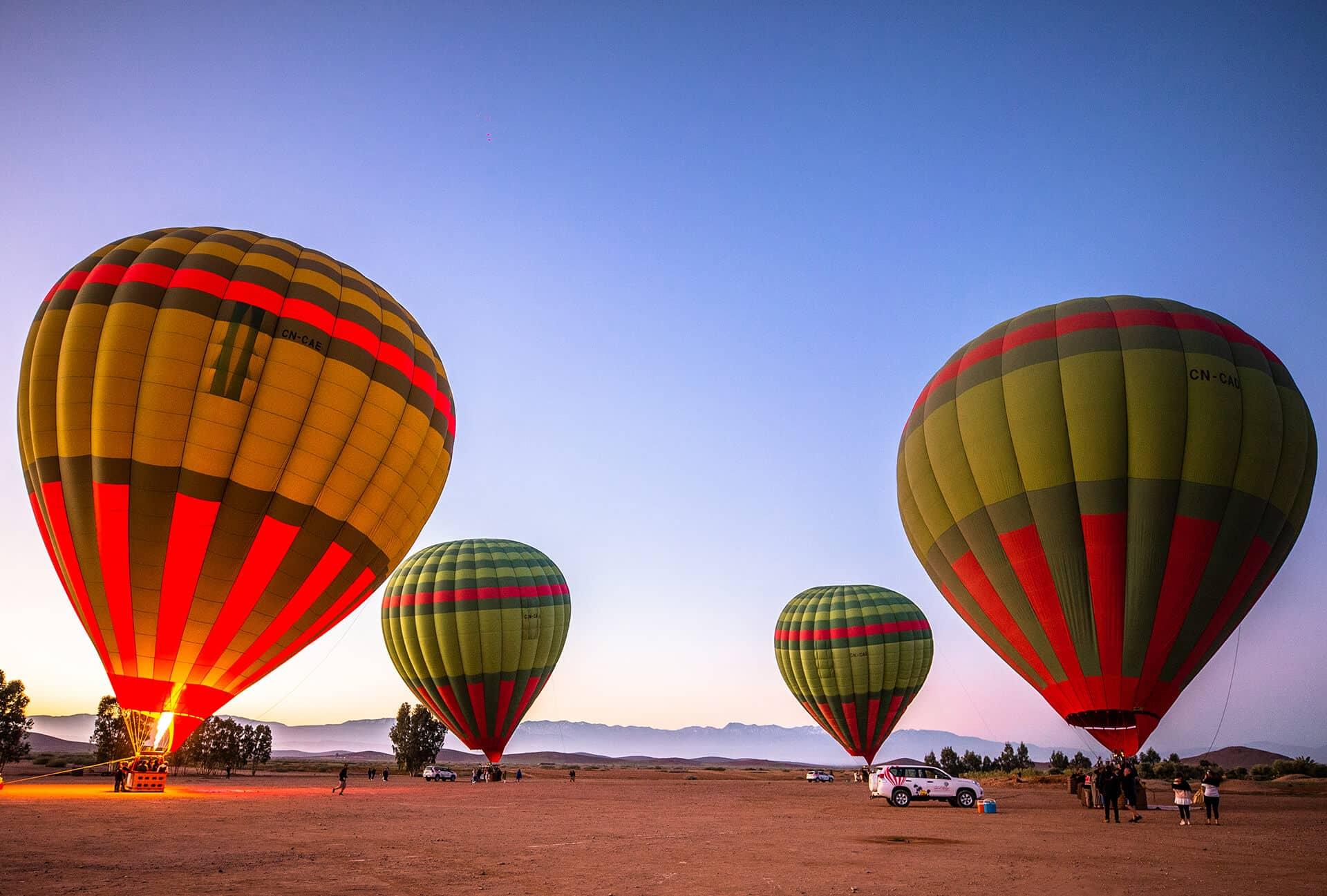 Hot air balloons, glowing with vibrant colors, prepare for liftoff against the backdrop of a clear blue sky.