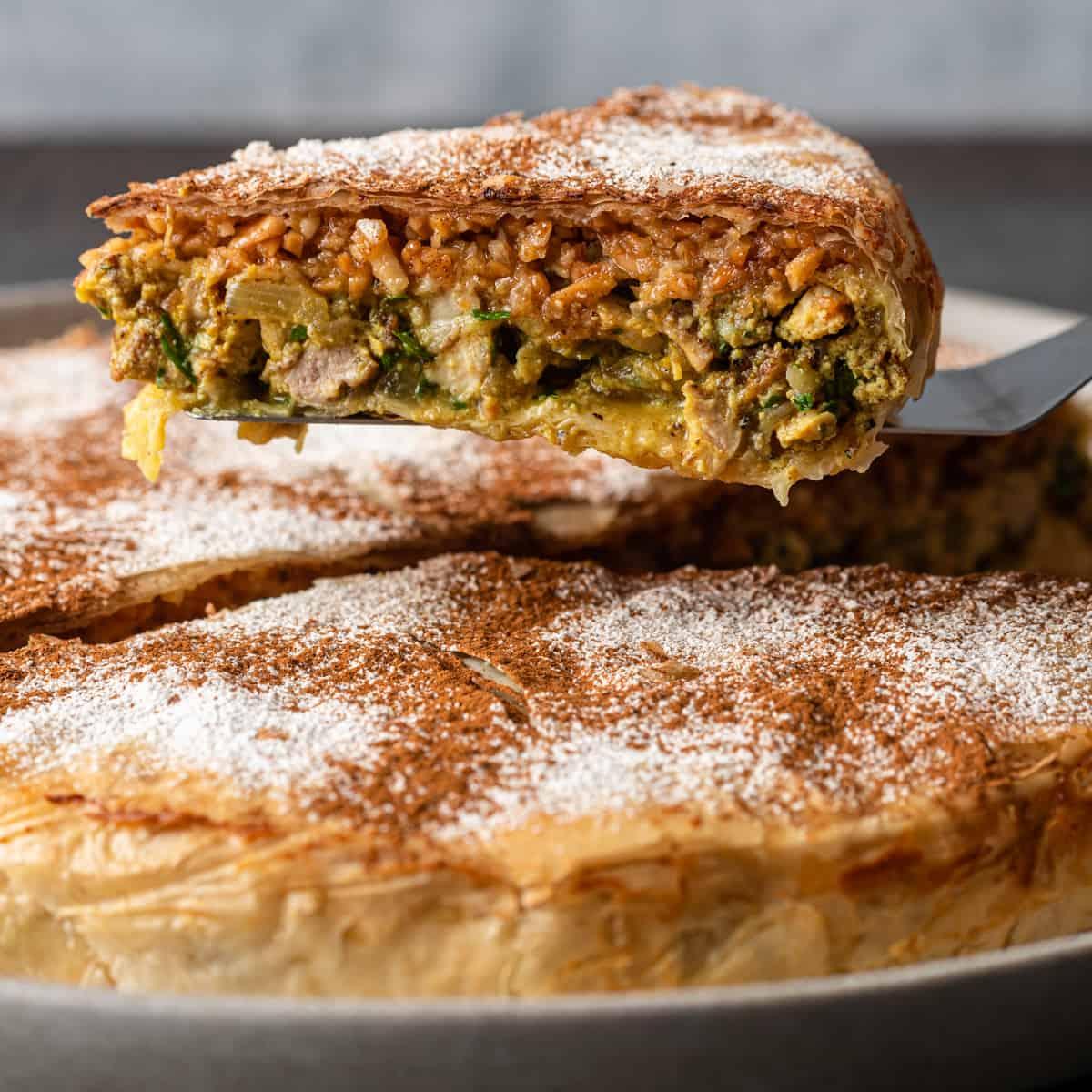 A slice of traditional Moroccan pastilla, featuring a savory filling encased in a flaky, golden pastry, dusted with powdered sugar and cinnamon.