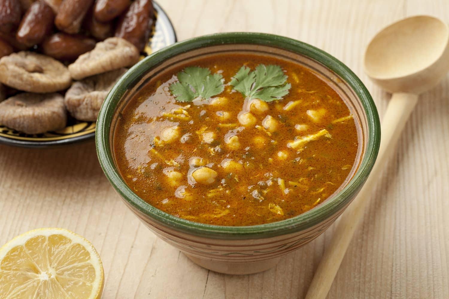 A bowl of traditional Moroccan harira, a hearty soup made with chickpeas, lentils, and fresh herbs, served with dates and dried figs.