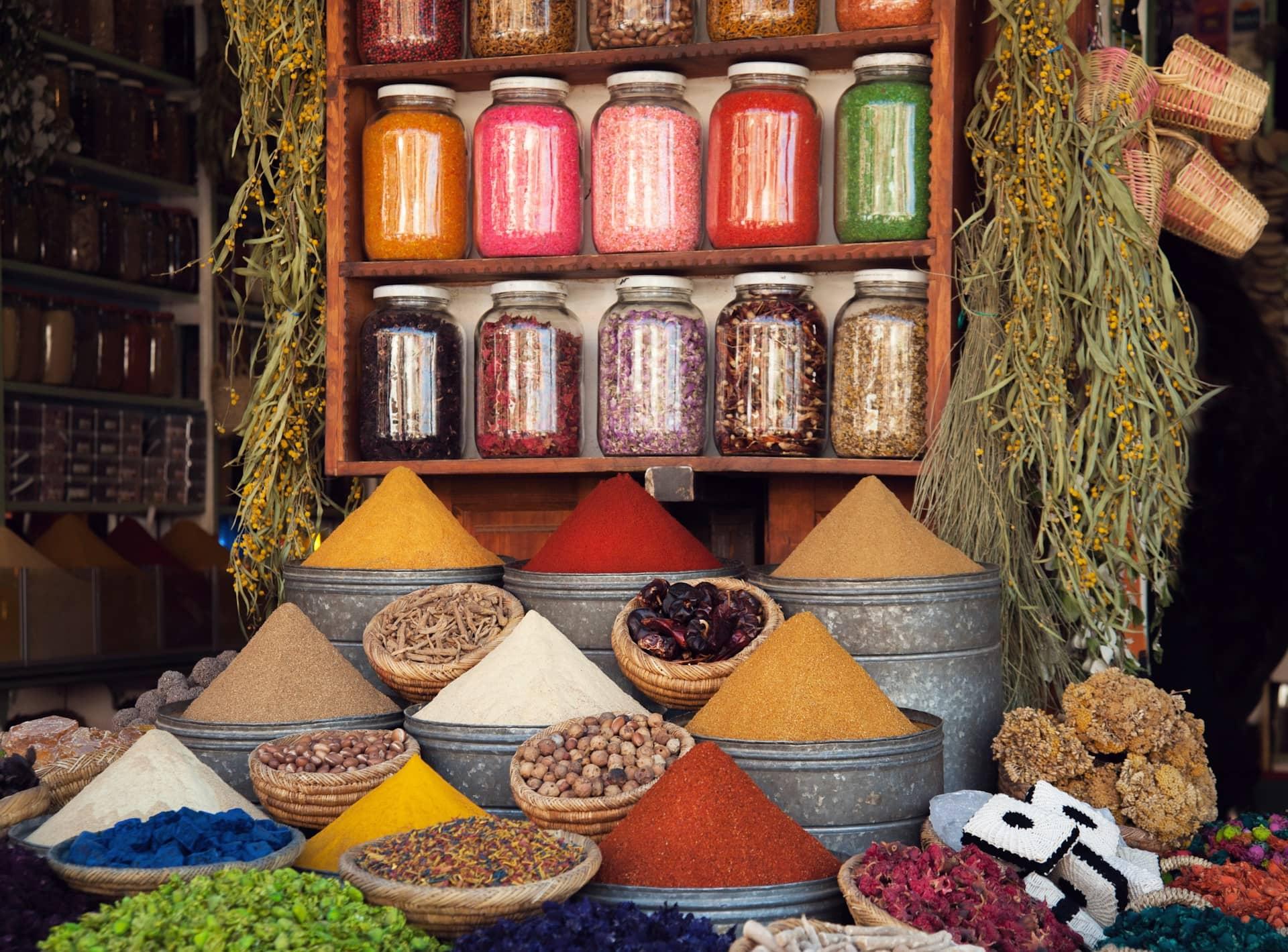 A vibrant display of spices and herbs in a Marrakesh market, featuring colorful powders and aromatic ingredients in baskets and jars.