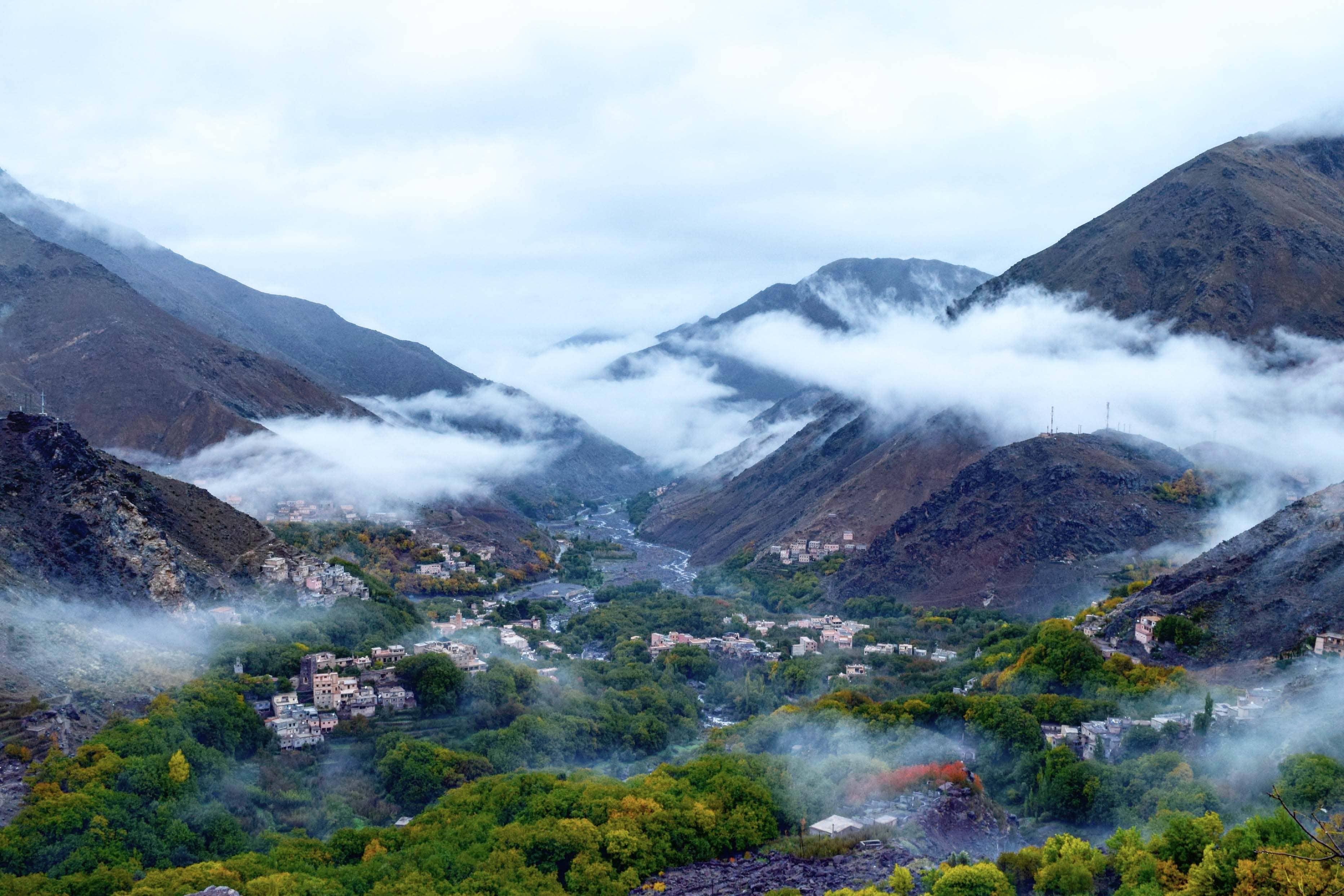 The High Atlas Mountains shrouded in mist with a village tucked into the green valley below.