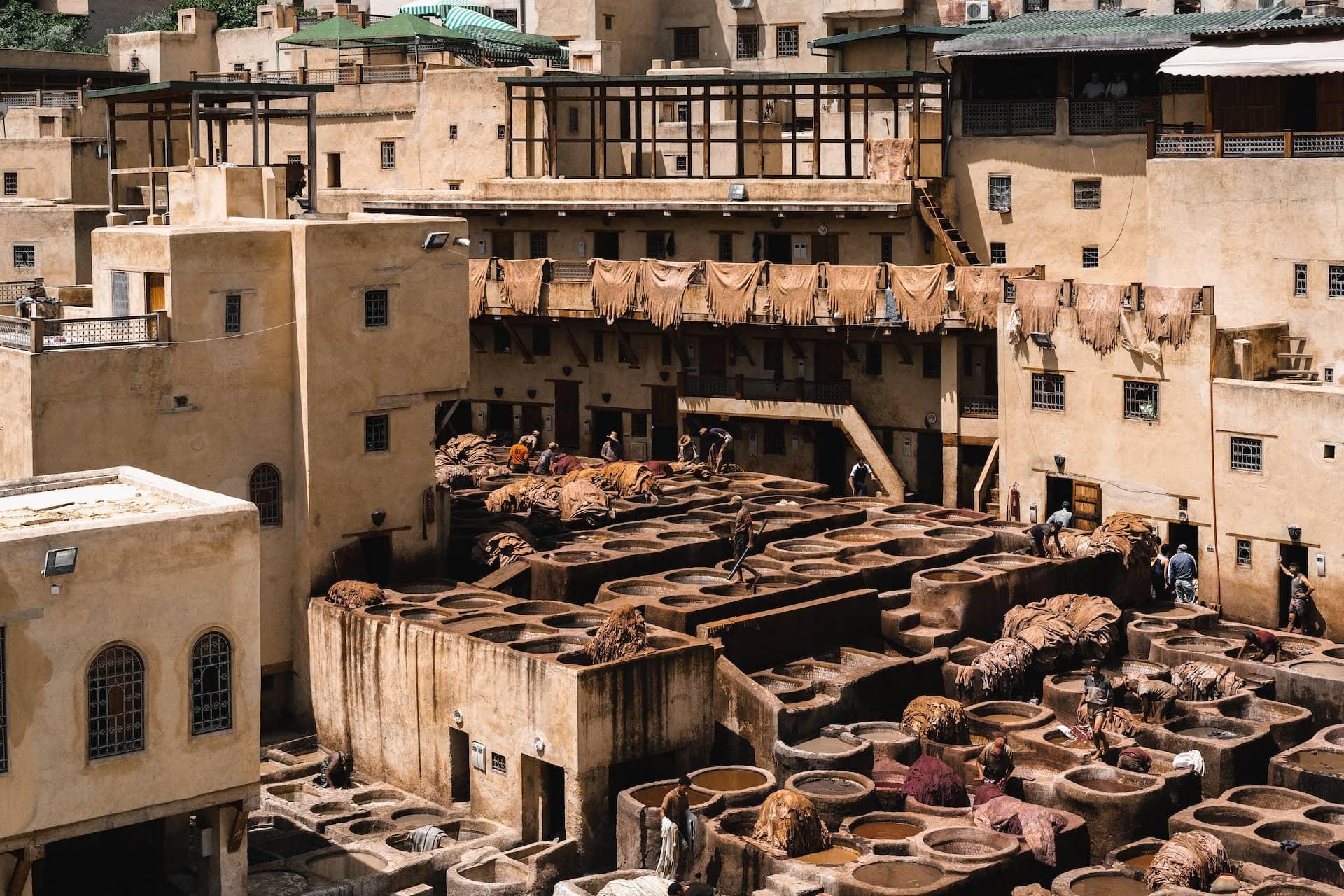 Traditional tanneries in Fes with workers dyeing leather amidst stone vats under the Moroccan sun.