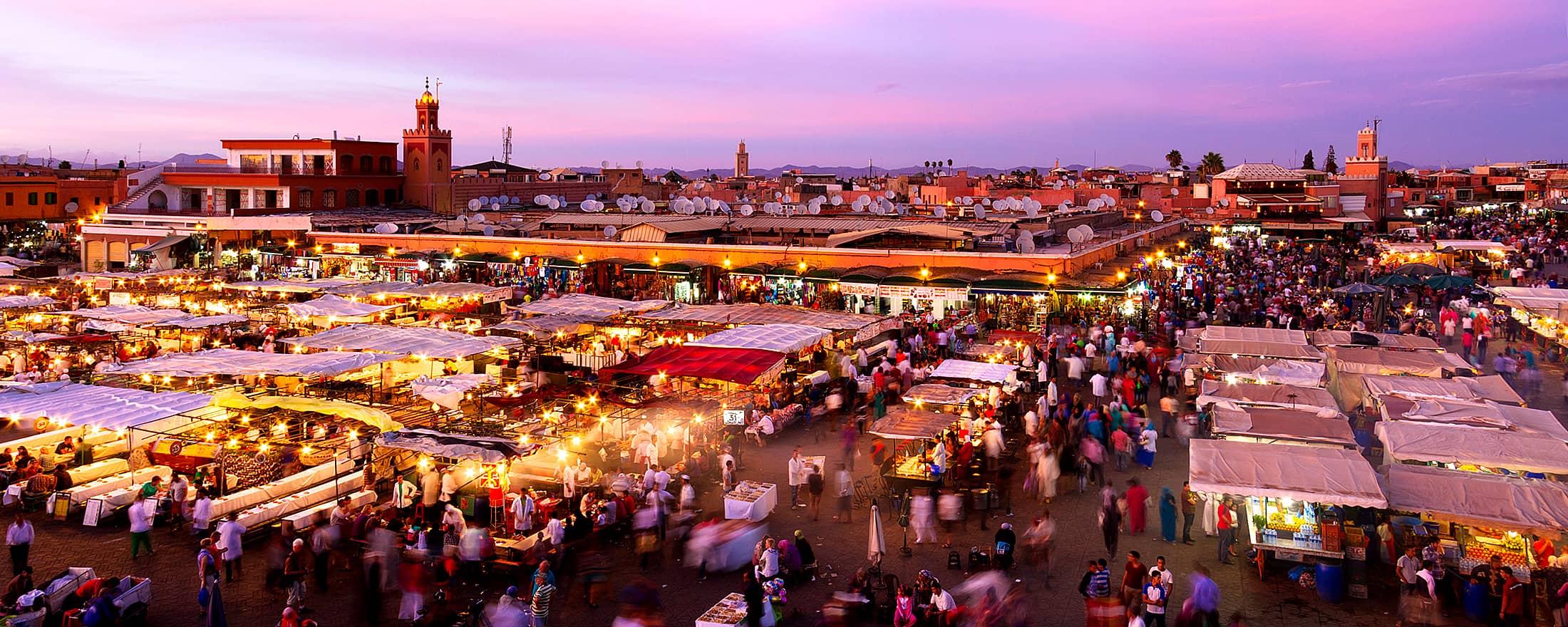 Dusk falls over Jemaa el-Fna in Marrakesh, illuminating the vibrant market stalls and bustling crowds.