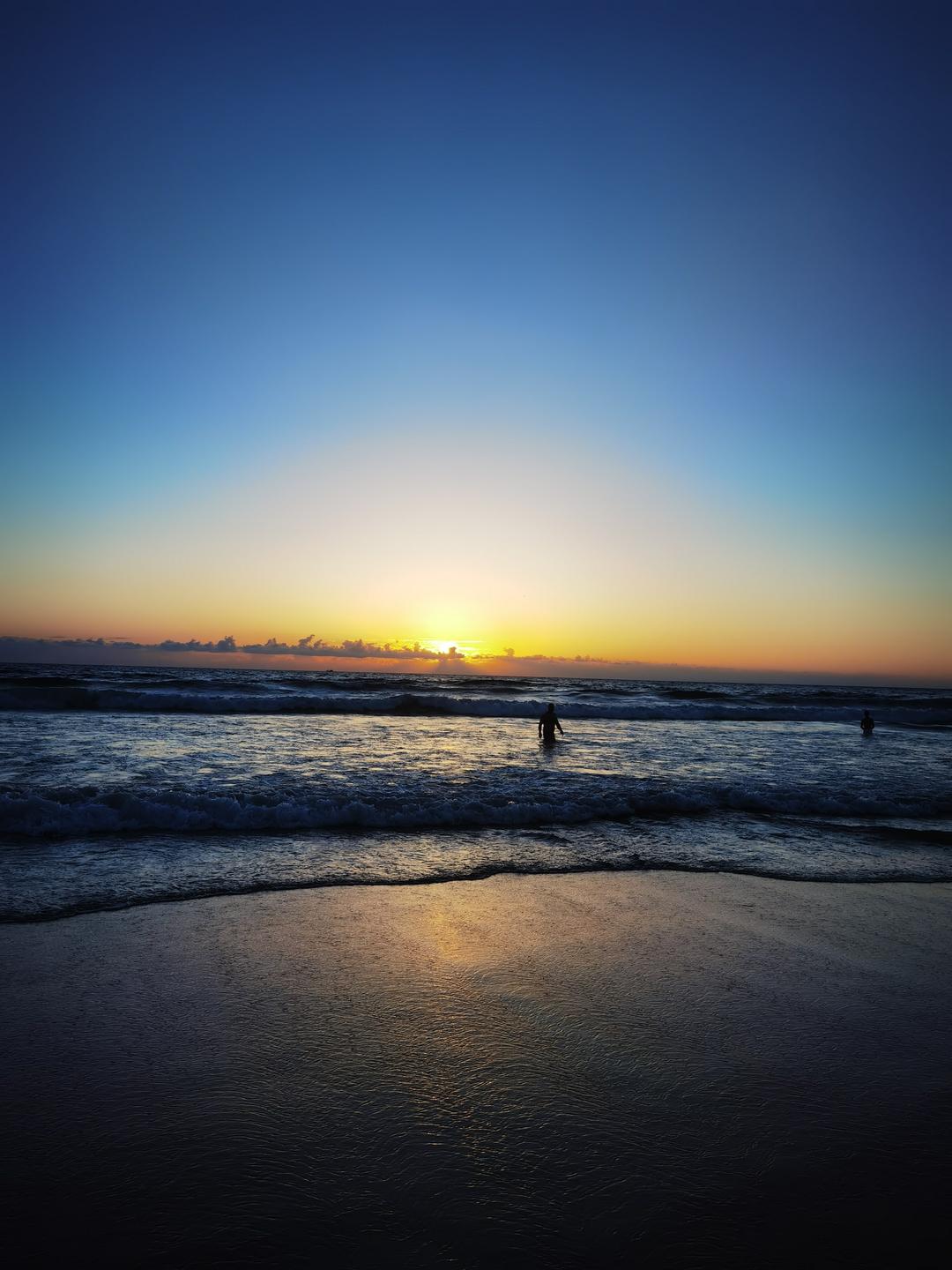  A breathtaking sunset over Tangier's beach, where the sun's final glow kisses the horizon, silhouetting figures in the gentle surf.